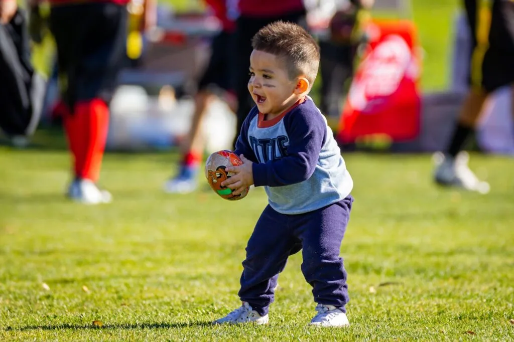 pexels-photo-3697601 - Ball to Life Sports Joyful toddler playing with a football on a sunny day outdoors, dressed in casual clothes.