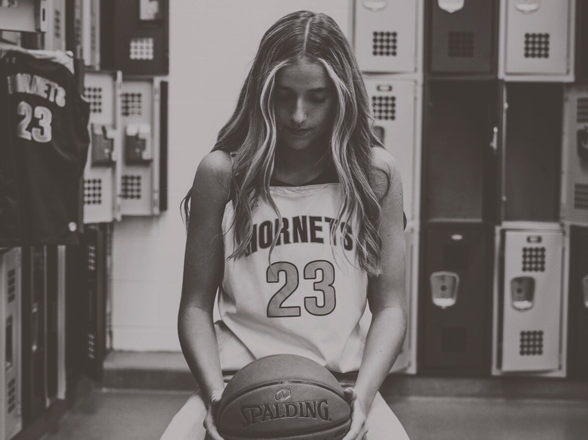 Upload up to 5 photos that you think should be shared as part of the Player Spotlight Min size 800 x 800 pixel IMG_0094 - Ball to Life Young woman in a basketball jersey with number 23 sits in a locker room, cradling a Spalding basketball.