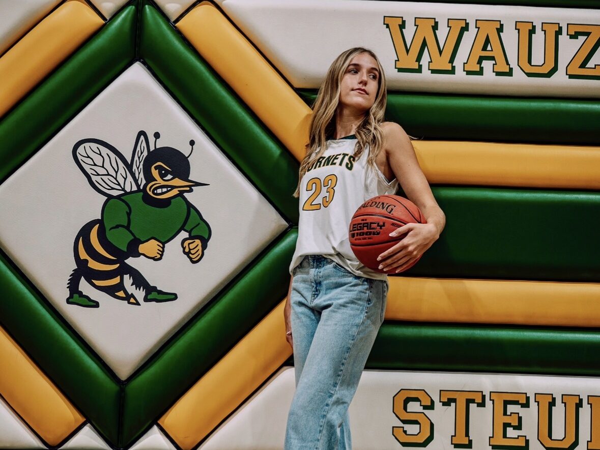 Upload up to 5 photos that you think should be shared as part of the Player Spotlight Min size 800 x 800 pixel IMG_0095 - Ball to Life Young woman in a Hornets jersey (#23) holds a basketball in a gym with a green-yellow padded wall and a hornet mascot mural behind her.